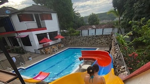 Ein Swimmingpool mit Wasserrutsche, umgeben von einer Steinmauer und viel Grün.