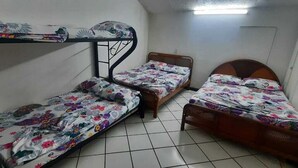 Ein Schlafsaalzimmer mit Stockbetten und einem Einzelbett, gefliestem Boden und einer Tür.