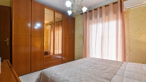 A bedroom with a large wardrobe, a bed with a patterned bedspread, and a window with curtains.
