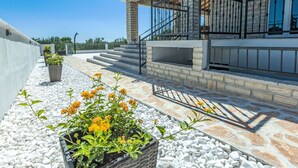 A modern building with a stone facade, a balcony with metal railings, and a pathway with white pebbles and yellow flowers. - Villa Šime by Interhome (Zadar/Sukošan)