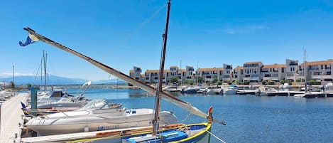 A marina with boats docked, a wooden pier, and buildings in the background.