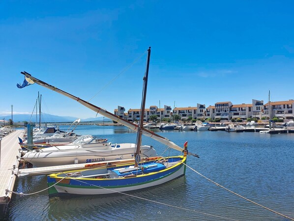 Un puerto deportivo con barcos amarrados, un muelle de madera y edificios al fondo.