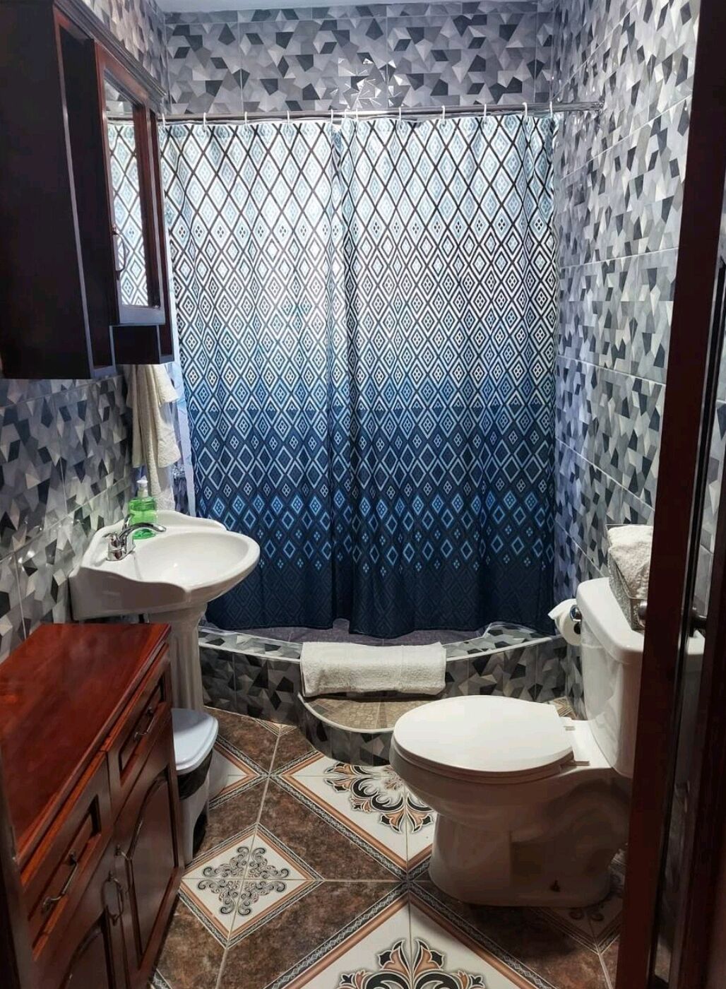 A bathroom with a patterned shower curtain, a sink, a toilet, and a vanity with drawers.