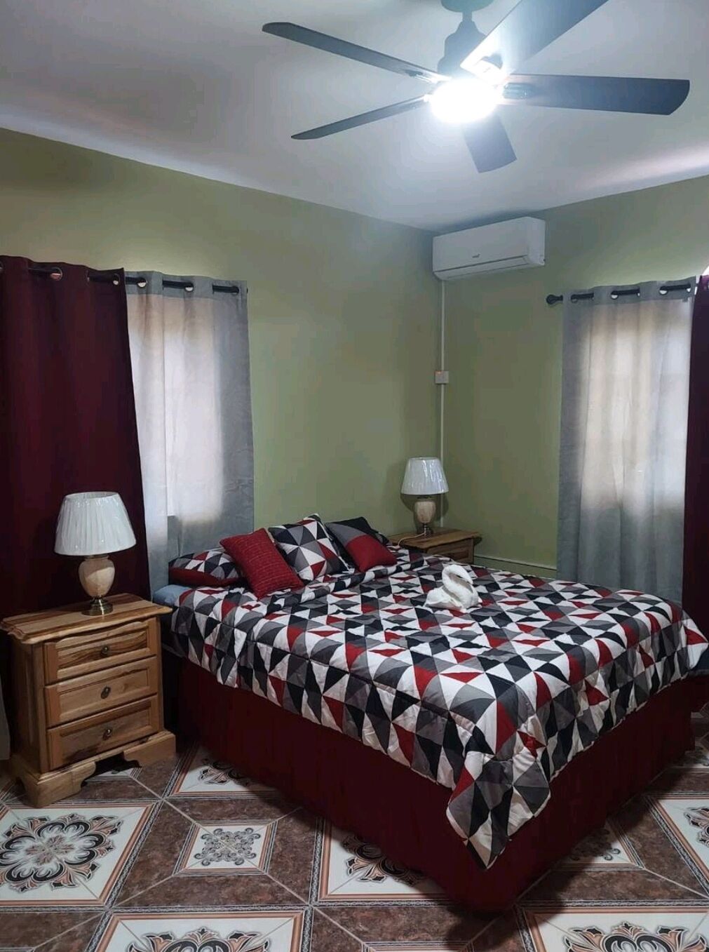 Un dormitori amb un llit, dues mesetes de nit, un ventilador de sostre i un aire condicionat fixat a la paret.
