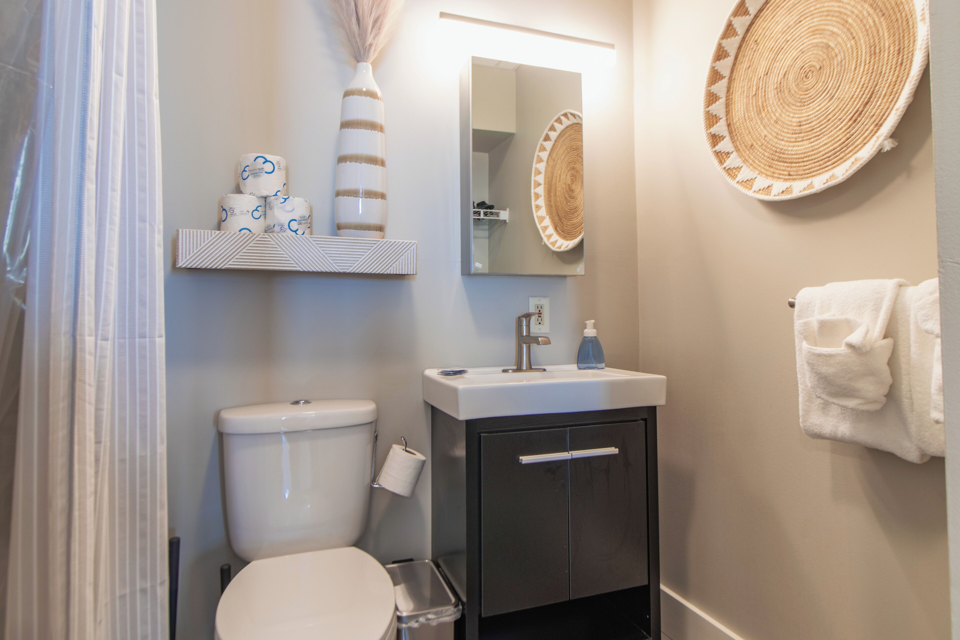A bathroom with a toilet, sink, and mirror. There is a towel rack with a towel hanging on it.