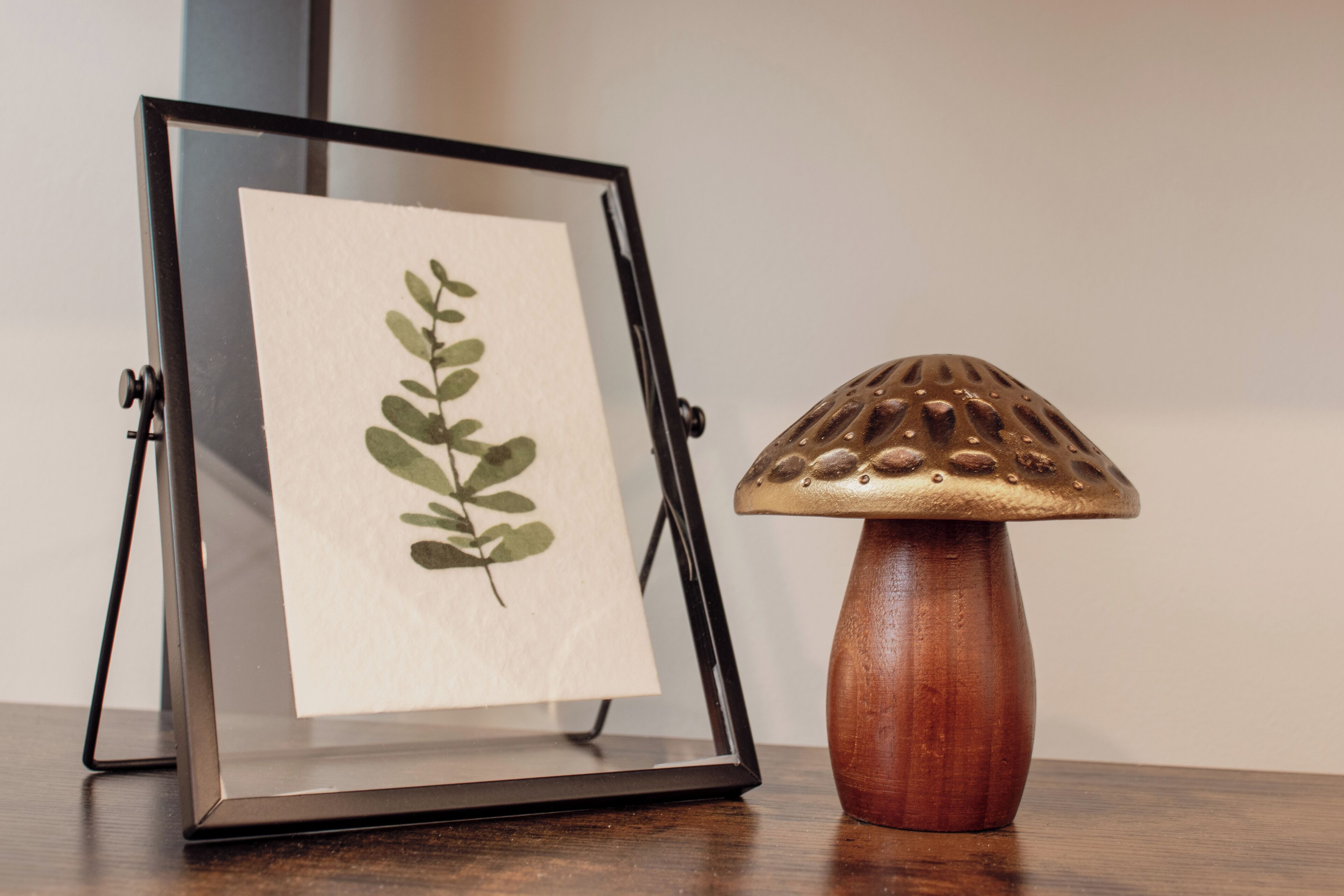A framed botanical print on a stand next to a wooden mushroom-shaped lamp.