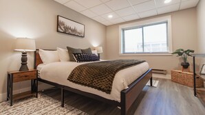 Een slaapkamer met een bed, twee nachtkastjes, een raam en een aan de muur bevestigd schilderij.