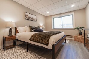 Une chambre à coucher avec un lit, deux tables de chevet, une fenêtre et un tableau accroché au mur.