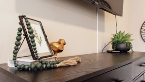 Een houten dressoir met een lijstfoto, een gouden vogelornament en een bloempot.