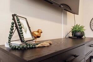 Une commode en bois ornée d’un tableau encadré, d’un petit oiseau décoratif en métal doré et d’une plante en pot.