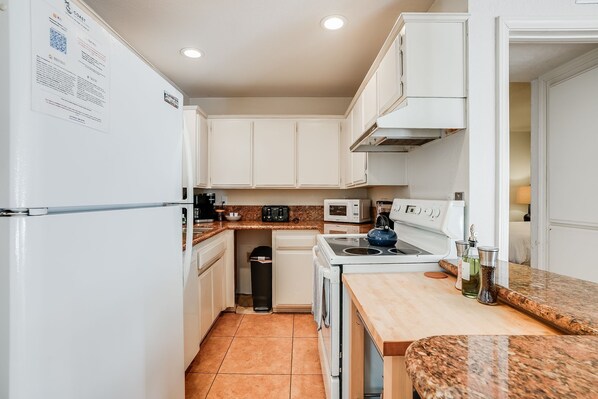 A modern kitchen with white cabinets, a granite countertop, a stove, and a trash bin.