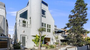 A modern, white building with a unique triangular shape, large windows, and a small balcony. - Massive Beach Home | Ocean View | Amazing Rooftop (San Diego)