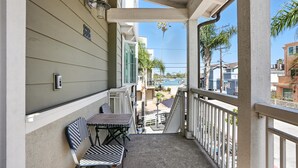 A balcony with a table and chairs, overlooking a residential area with a view of a beach and houses. - Steps to Water - Newly Built Bayside Dream | Patios, Fire Pit, Bay Views, Garage (San Diego)