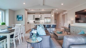 A spacious living area with a modern kitchen, a dining table, and comfortable seating. - Steps to Water - Newly Built Bayside Dream | Patios, Fire Pit, Bay Views, Garage (San Diego)