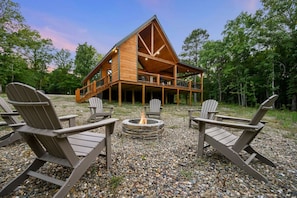Eine Holzhütte mit Feuerstelle aus Stein, einer Holzterrasse und Adirondack-Stühlen.