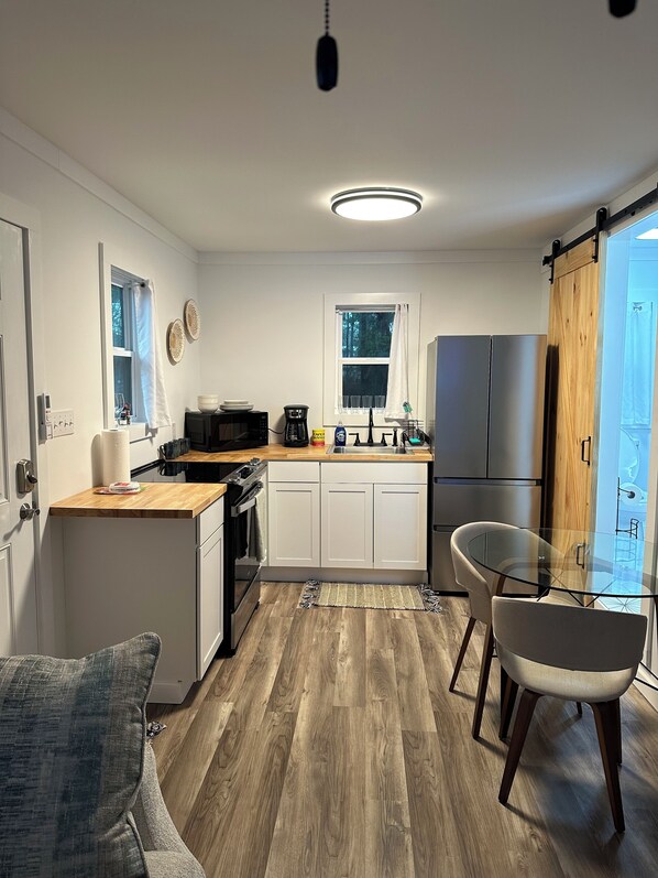 A modern kitchen with white cabinets, a wooden countertop, a glass table, and a sliding wooden door.