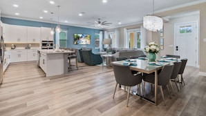 A modern kitchen with white cabinets, a central island, and a dining area with a glass table and chairs. - Villa Miramar | Luxury 7-Bedroom Villa at Reunion Resort (Kissimmee)