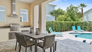 An outdoor patio with a grill, dining table, and chairs, a swimming pool, and lounge chairs. - Villa Miramar | Luxury 7-Bedroom Villa at Reunion Resort (Kissimmee)