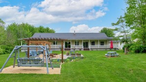 Ein Haus mit überdachter Veranda, einer Schaukel und einem Picknicktisch im Garten.