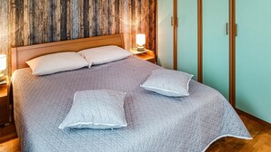 Ein ordentlich bezogenes Bett mit einer grauen Steude, zwei Kissen und einer Nachttischlampe.