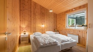 Ein Schlafzimmer mit Holzwandverkleidung, einem Bett, Nachttischen, einem Fenster und einer Heizung.
