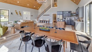 A spacious open-plan living area with a wooden dining table, black chairs, a staircase, and a kitchen with grey cabinets.