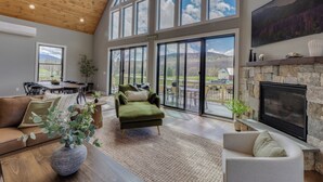 A spacious living room with a high ceiling, large windows, a fireplace, and a dining area.