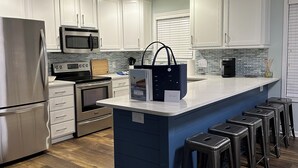 Een moderne keuken met witte kasten, roestvrijstalen apparatuur, een blauw kookeiland met barkrukken en een visgraat houten vloer.
