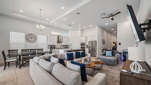 A spacious living room with a large sectional sofa, a dining area with a wooden table and chairs, and a kitchen with modern appliances. - Liberty Grandview: Private Pool, Water Park, Golf Views (Kissimmee)
