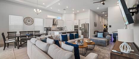 A spacious living room with a large sectional sofa, a dining area with a wooden table and chairs, and a kitchen with modern appliances.
