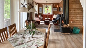 A cozy living room with a fireplace, wooden walls, and a dining area with a table set for two. - 3 bedroom lovely home in Sandnes (Sandnes)