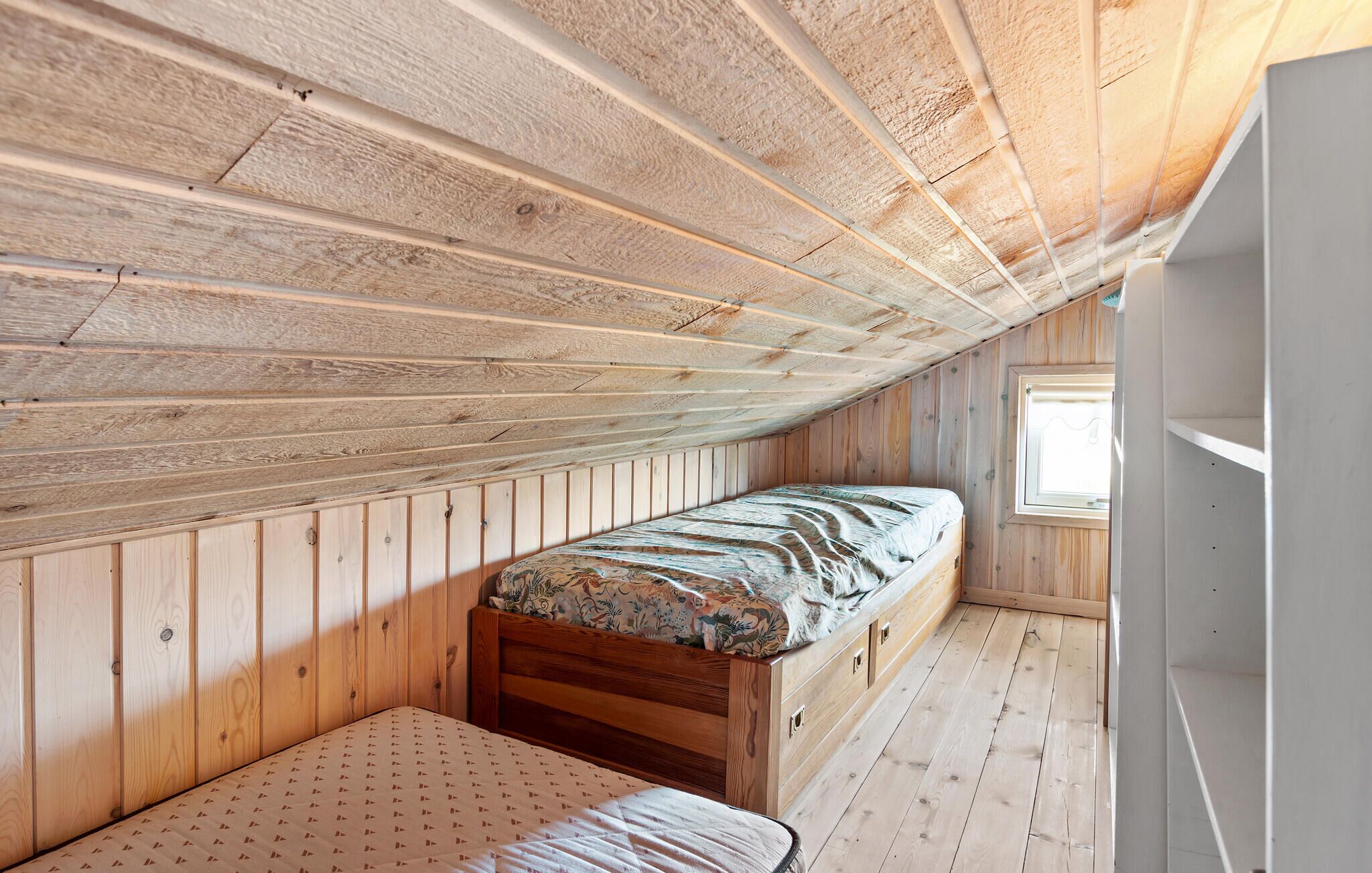 A small, wooden attic bedroom with a single bed and a window.