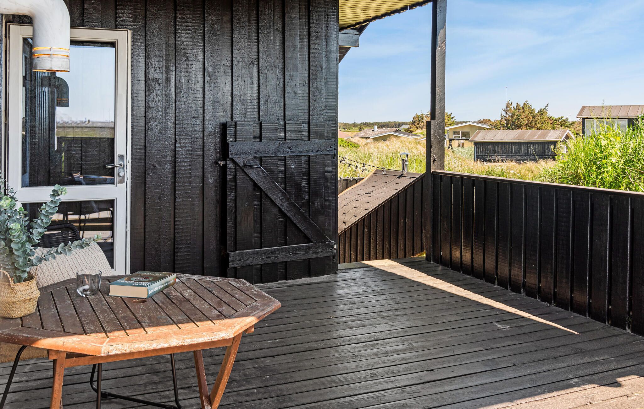 A wooden deck with a table and chairs, a black gate, and a view of the surrounding area.