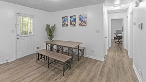 A dining area with a wooden table and benches, a potted plant, and three framed pictures on the wall.
