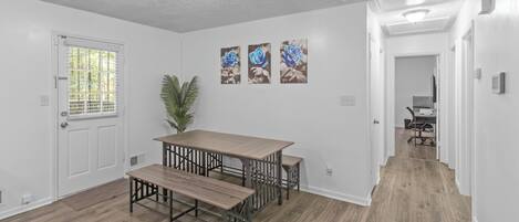 Un comedor con una mesa de madera y bancos, una planta en maceta y tres cuadros en la pared.