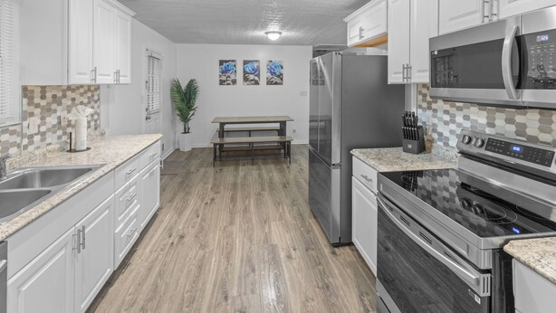 A modern kitchen with white cabinets, a stainless steel refrigerator, a microwave, and an oven.