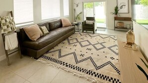 Un salon spacieux avec un canapé en cuir marron foncé, un tapis à motifs et un ventilateur de plafond.