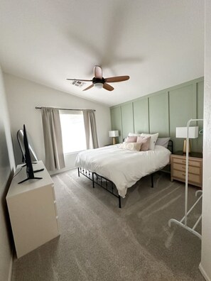 A bedroom with a bed, a desk, a chair, a ceiling fan, a window with curtains, and a nightstand with a lamp. - Mesa Oasis | Patio | Spacious | Central | Garage (Mesa)