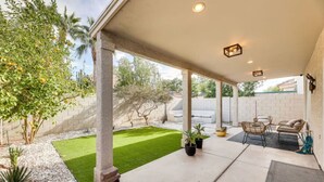 Un patio couvert avec une petite pelouse, un espace salon et des plantes en pot.
