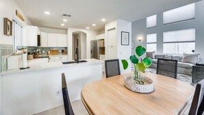 Une cuisine moderne avec des meubles blancs, un îlot central et un coin repas comprenant une table et des chaises en bois.