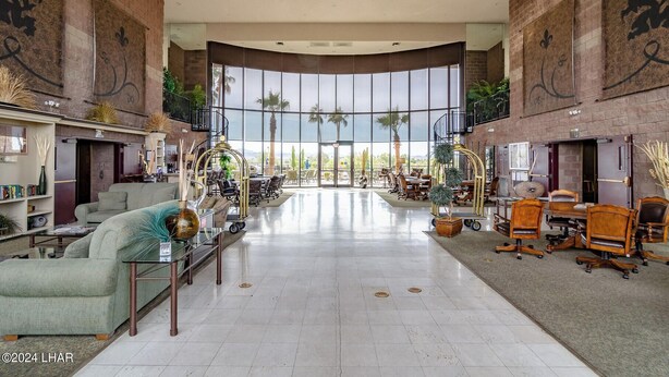 A spacious lobby with a curved ceiling, large windows offering views of palm trees, and a variety of seating arrangements including sofas and chairs.