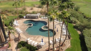 A resort with a swimming pool, lounge chairs, and a view of mountains and a lake.