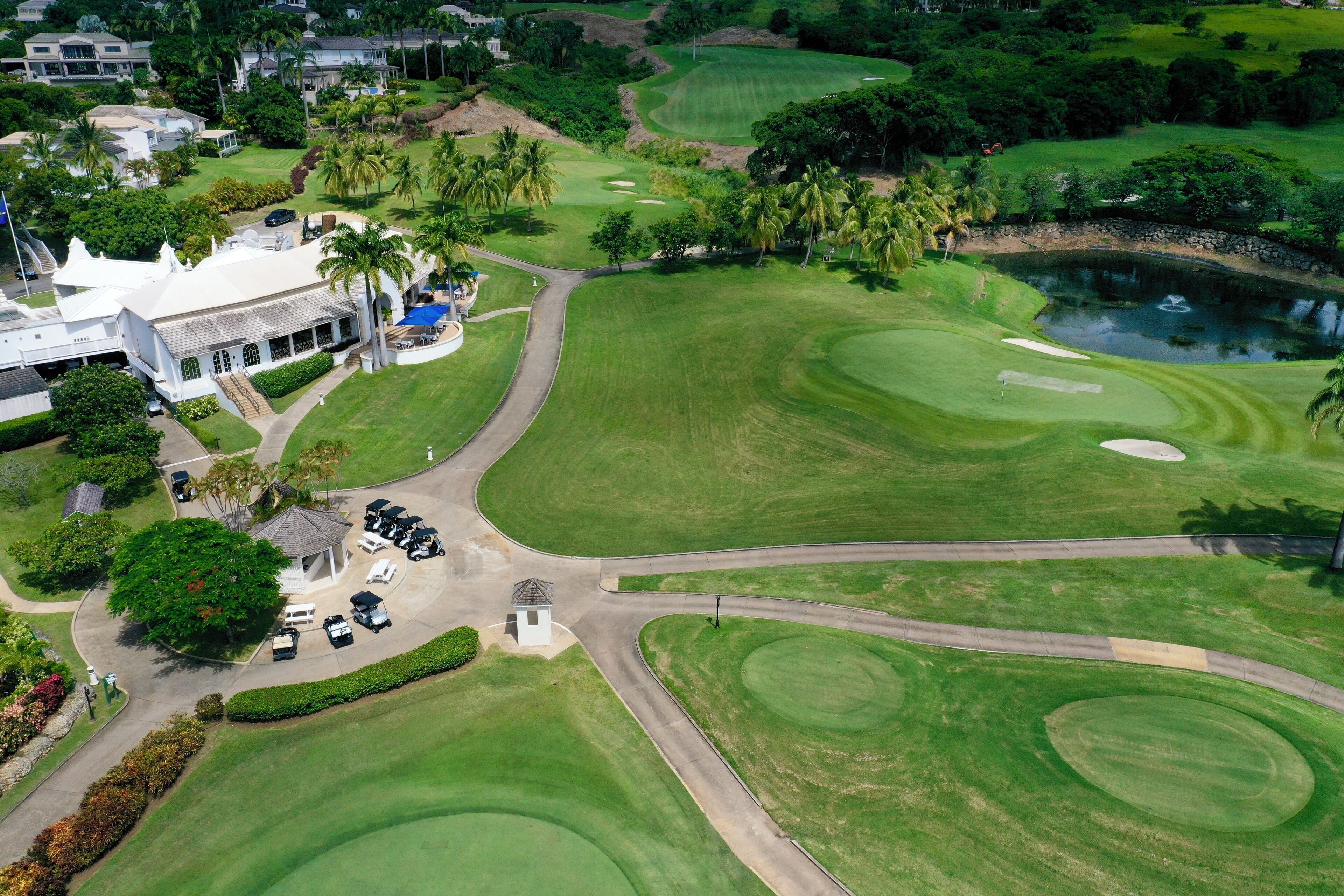 A golf course with a clubhouse, parking area, and a pond.