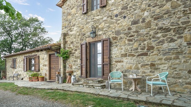 A stone building with a rustic exterior, featuring a small outdoor seating area with two chairs and a table.