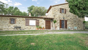 A stone building with a rustic exterior, featuring a large window, a door, and a small porch area with a bench and potted plants.