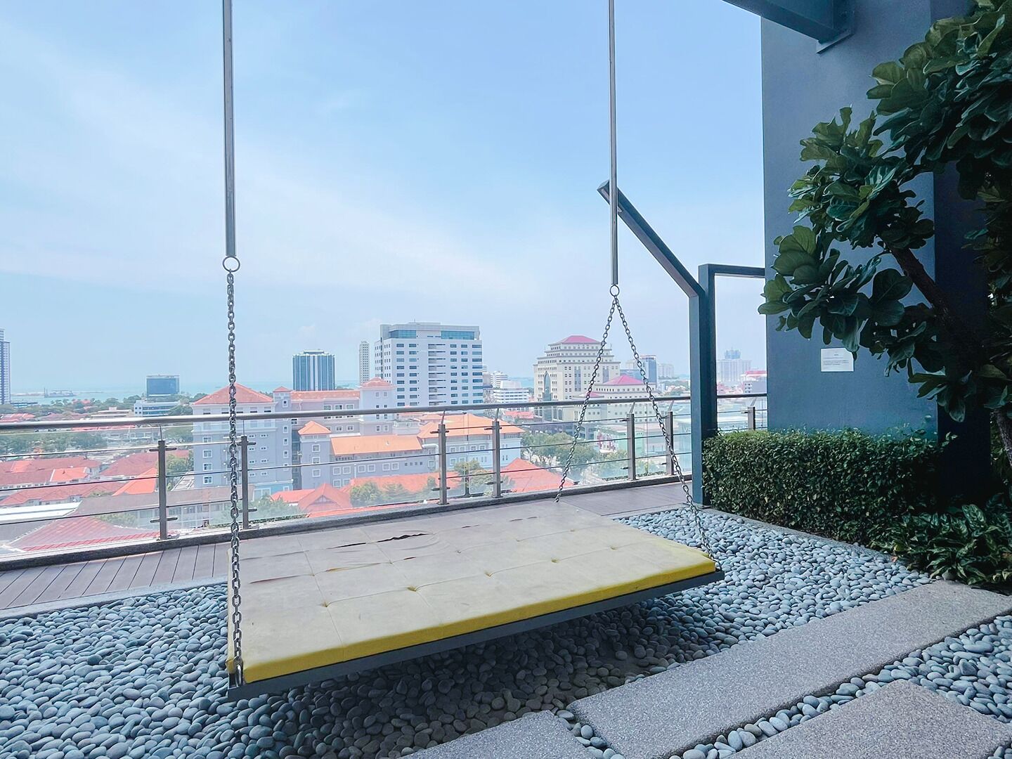 A swing chair with a yellow seat and metal frame, overlooking a cityscape with buildings and a body of water.