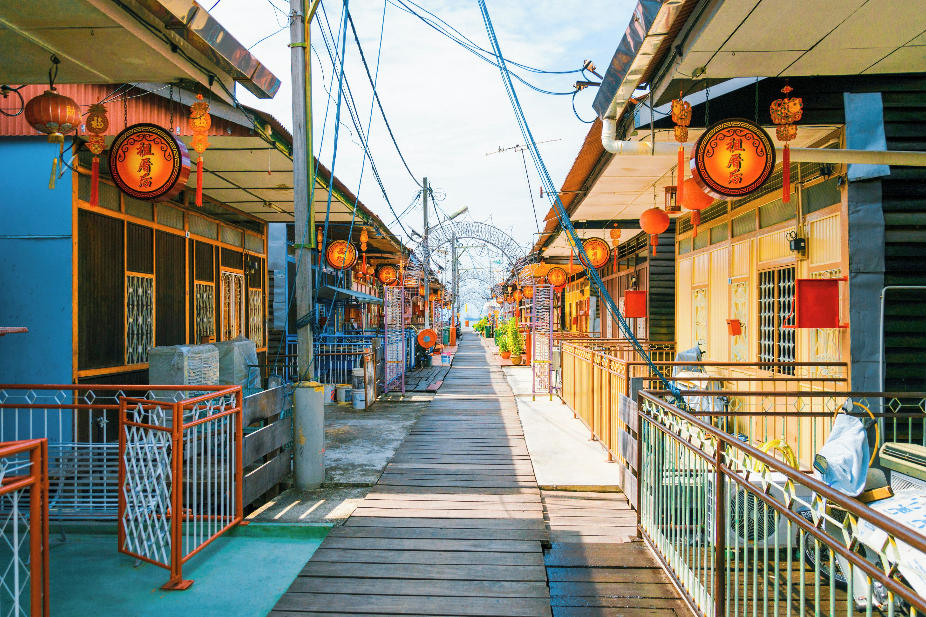 A narrow wooden pathway flanked by buildings with traditional Chinese architecture, including red lanterns and signage.
