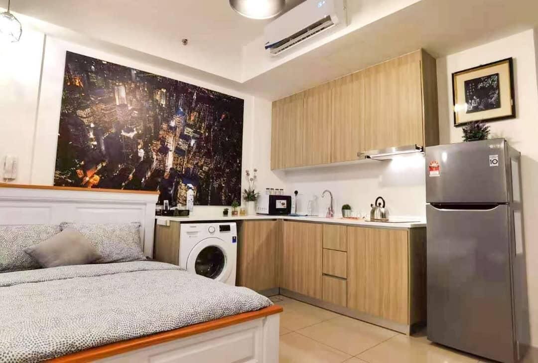Un ambiente compatto con letto, lavatrice, angolo cottura e un'ampia pittura astratta appesa al muro.