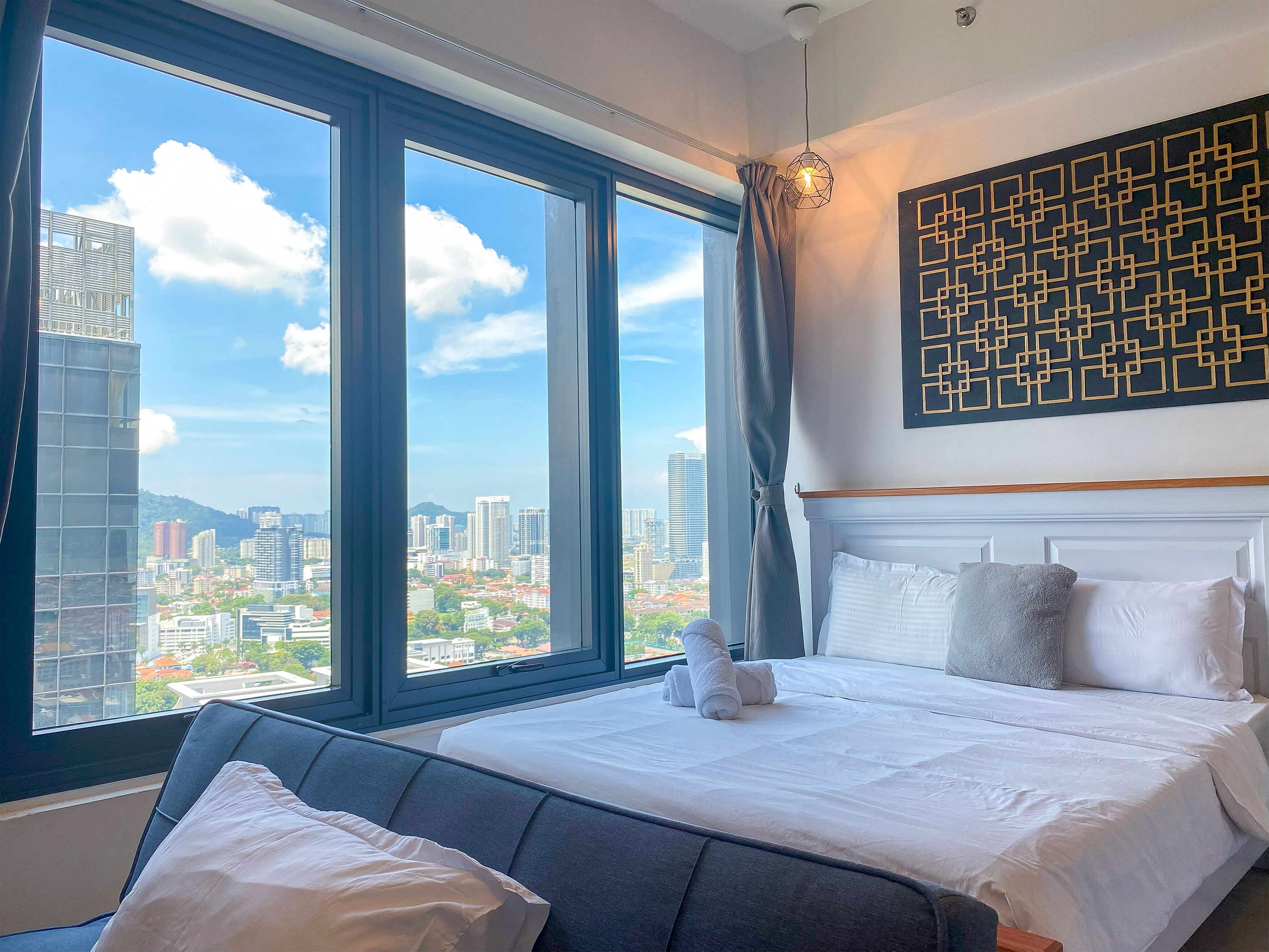 A hotel room with a large bed, a view of the cityscape, and a geometric wall art piece.