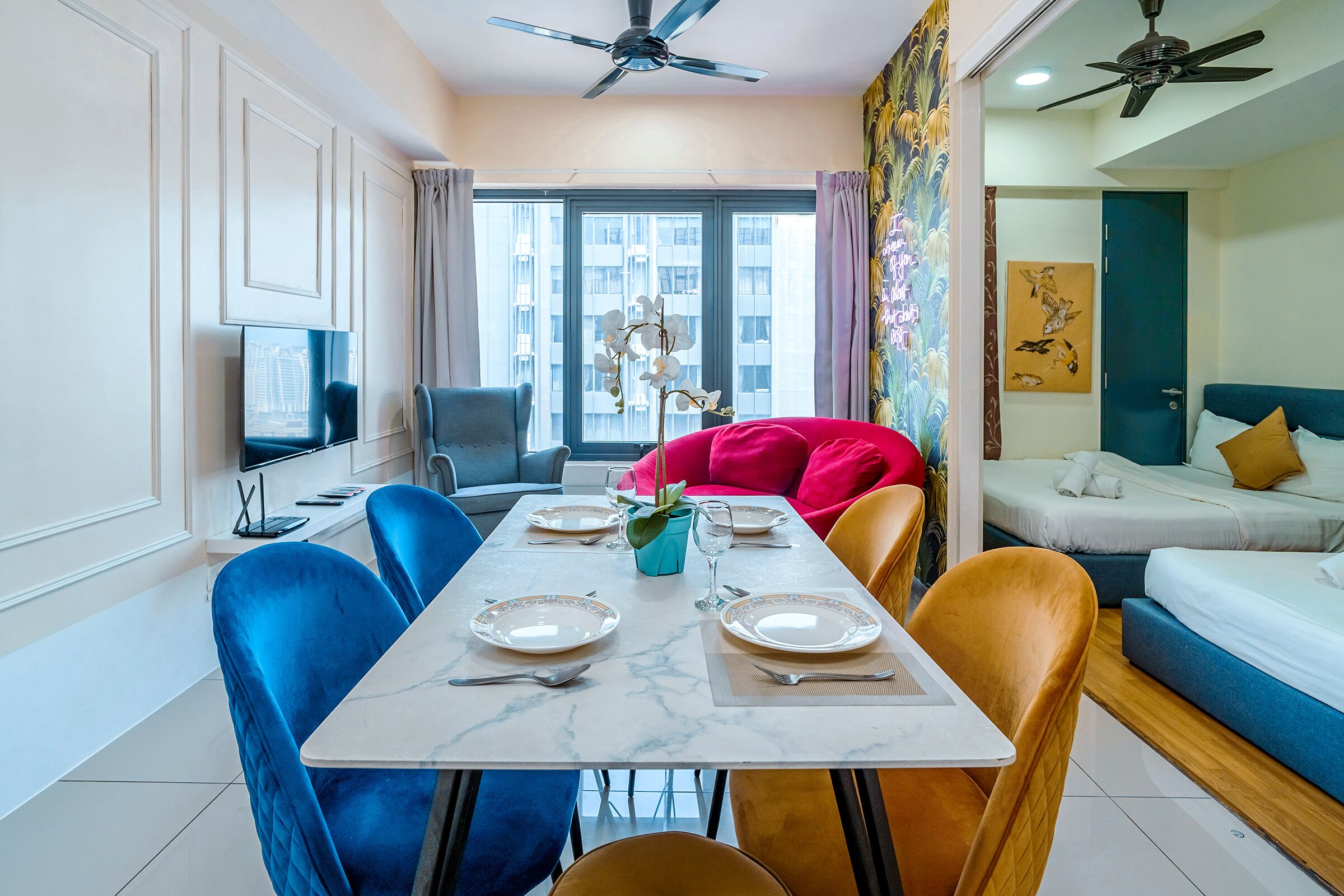A modern living room with a dining area, a TV, and a large window with a view of buildings.